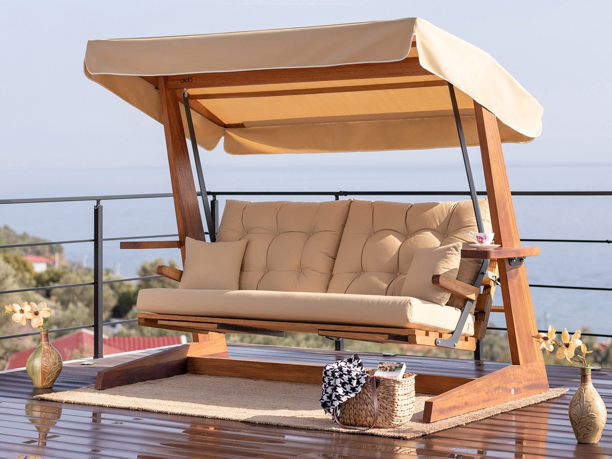 Luxe houten schommelbank met beige kussens op een terras met zeezicht